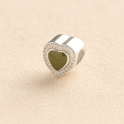 Heart-shaped silver ashes charm with a sage resin infill on a beige background