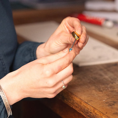 Close-up of hands holding a small self fill urn tools on a wooden surface