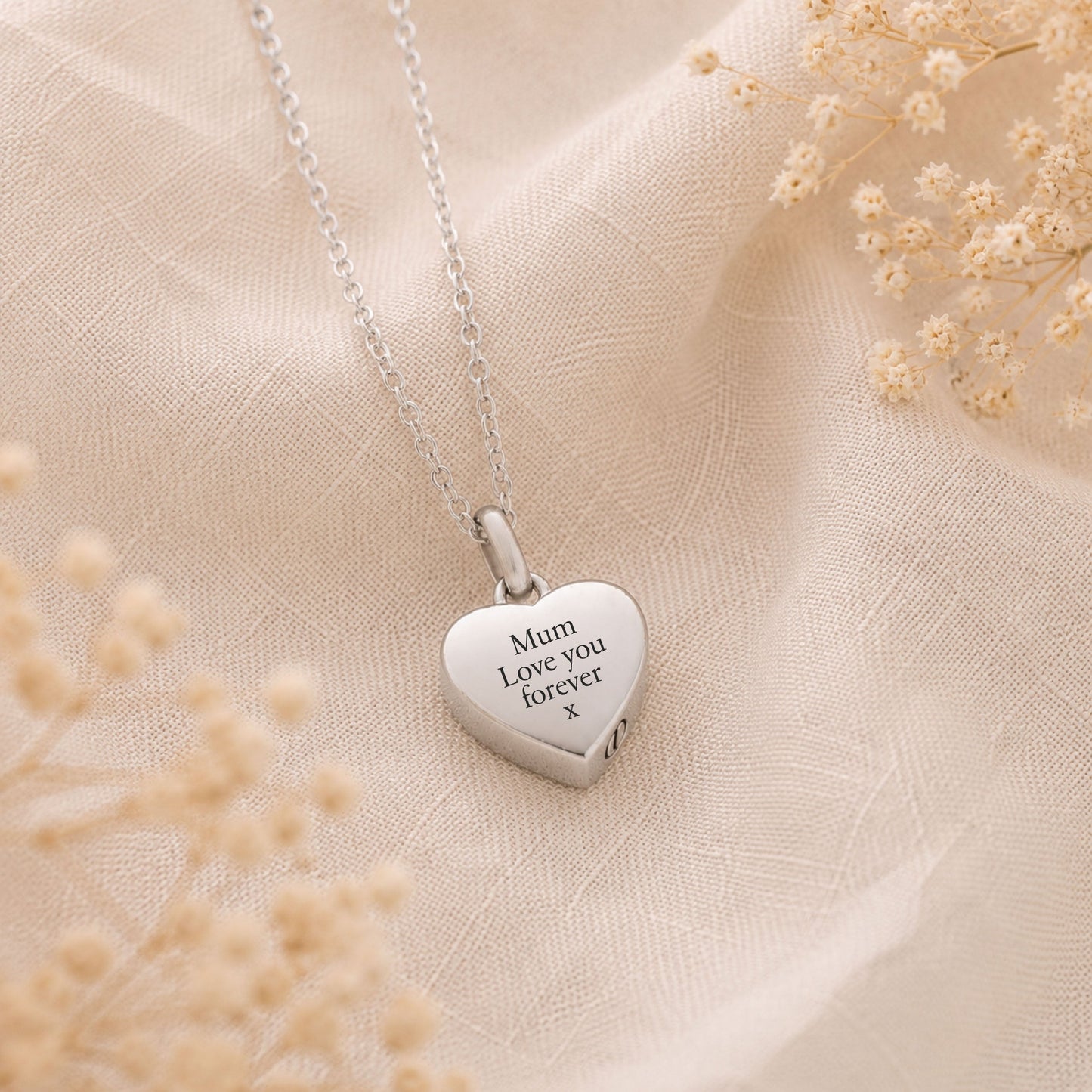 Silver heart-shaped pendant memorial necklace with engraved text on a beige fabric background