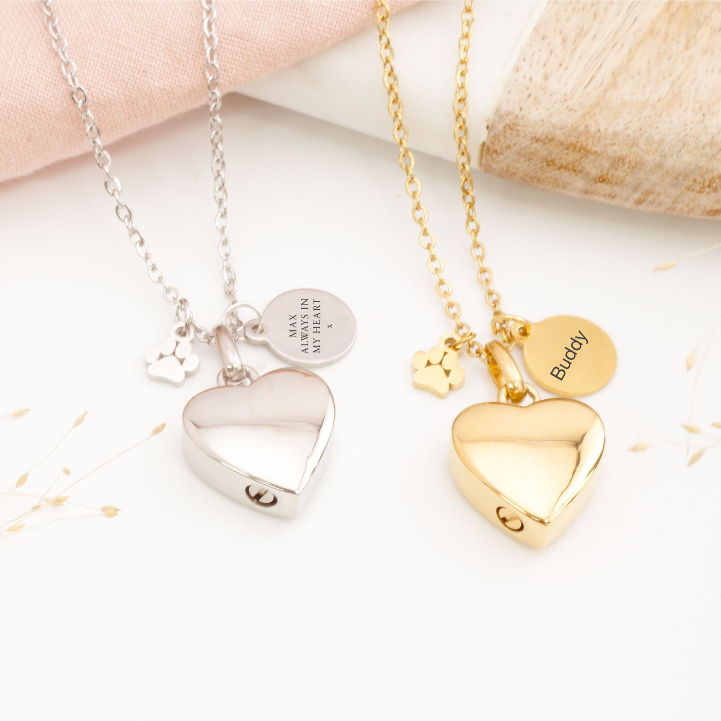 Two heart-shaped pet memorial necklaces, one silver and one gold, on a light background.