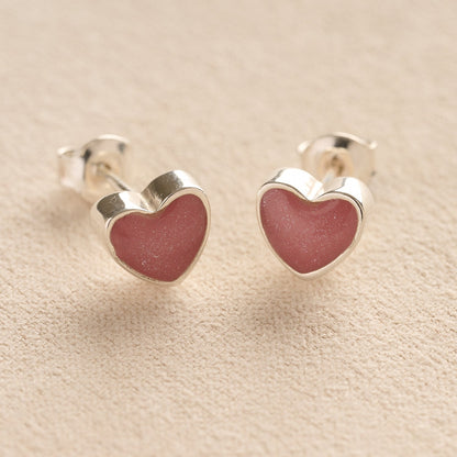 Silver Heart-shaped memorial earrings with dark pink resin with cremation ashes or fur a beige fabric background