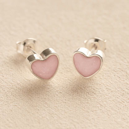 Silver Heart-shaped ashes earrings with light pink resin with cremation ashes or fur a beige fabric background