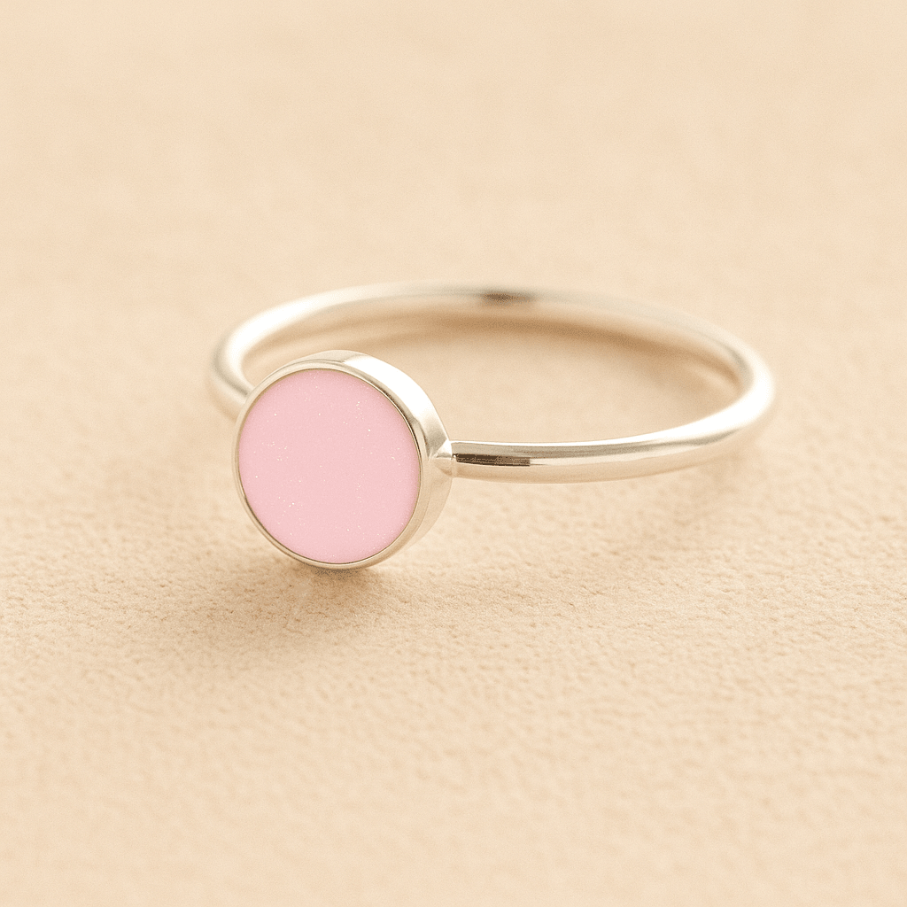 Sterling Silver ashes ring with a light pink resin circle filled with ashes or fur on a beige background