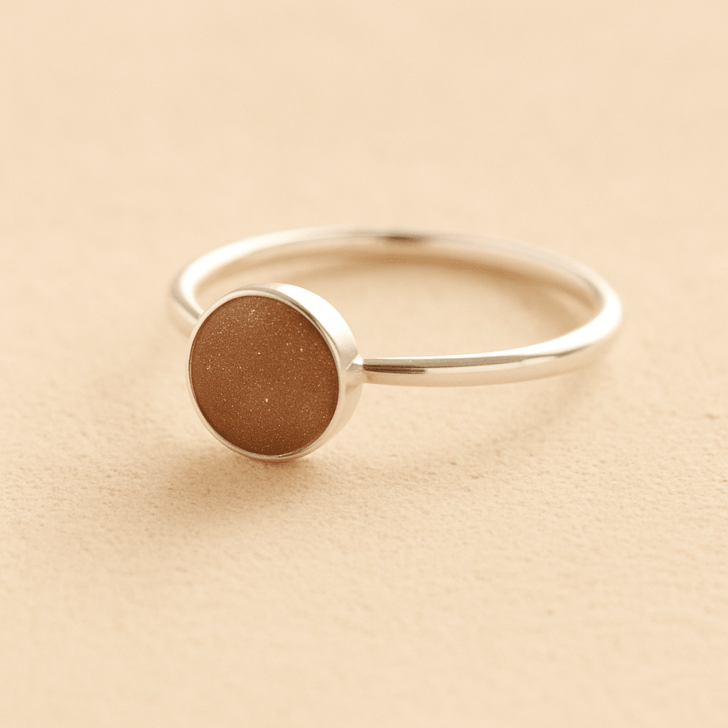 Sterling Silver ashes ring with a mocha brown resin circle filled with ashes or fur on a beige background