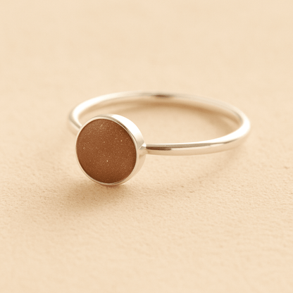 Sterling Silver ashes ring with a mocha brown resin circle filled with ashes or fur on a beige background