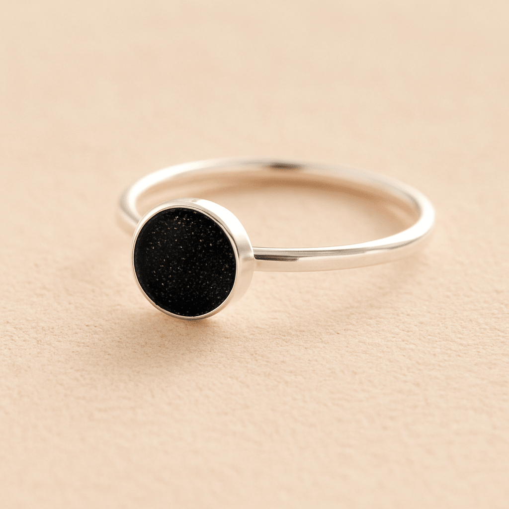 Silver cremation ashes ring with a black resin circle bezel filled with ashes or fur on a beige background