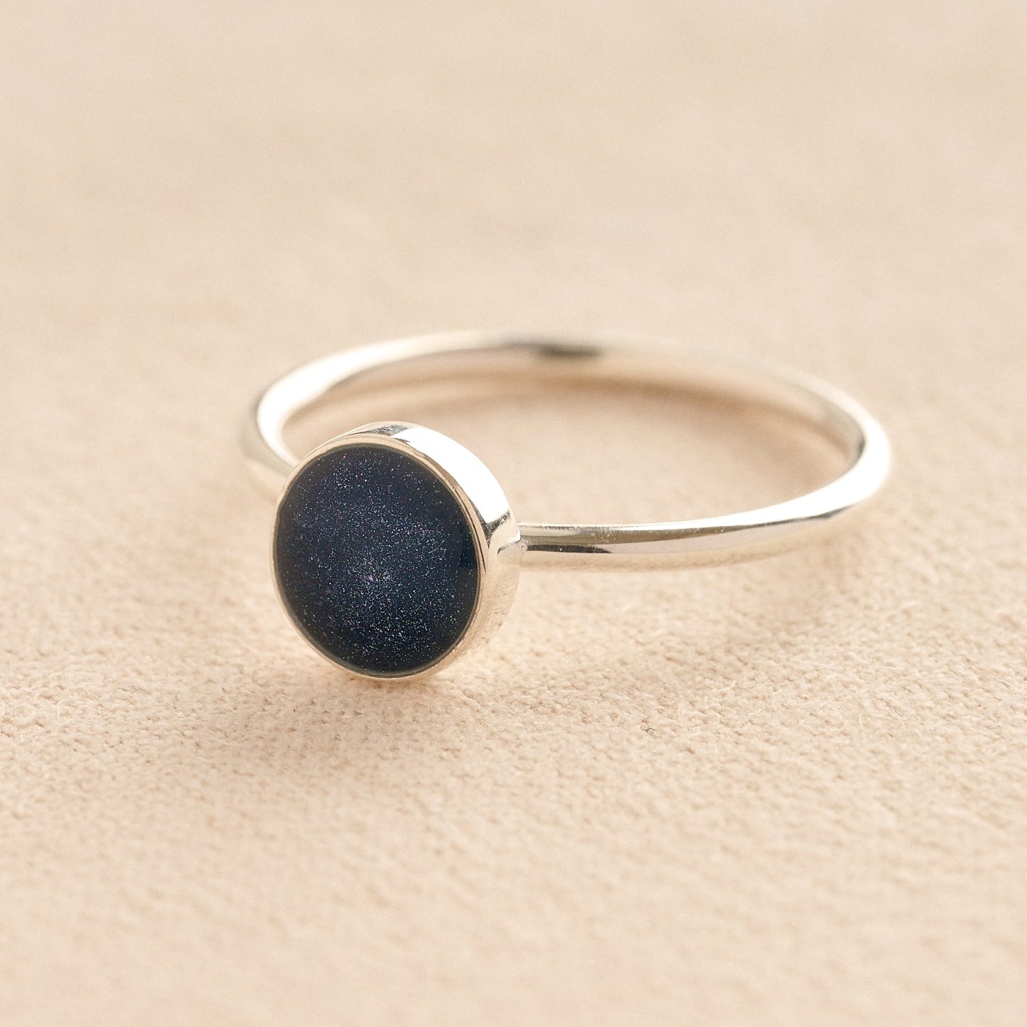 Silver memorial ashes ring with a navy resin circle bezel on a beige background