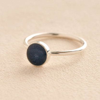 Silver memorial ashes ring with a navy resin circle bezel on a beige background