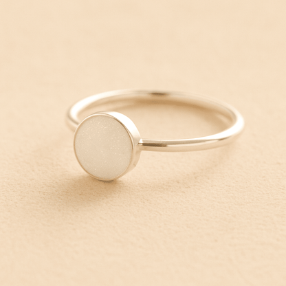 Silver cremation ashes ring with a white resin circle bezel filled with ashes or fur on a beige background