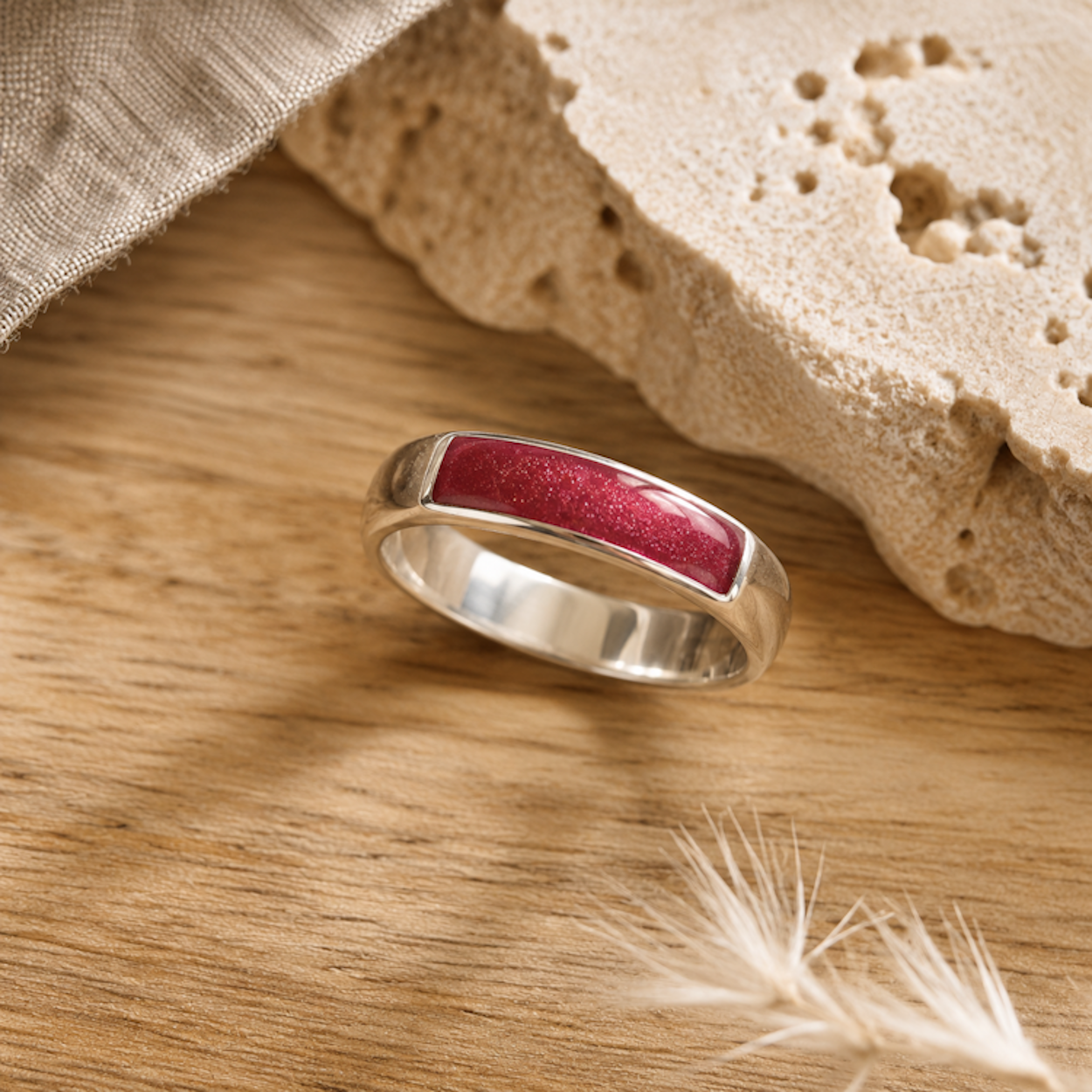 Silver mens ashes ring with dark pink resin inset for ashes, fur and hair on a wooden surface with a stone and feather.