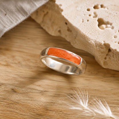 Silver mens ashes ring with orange resin inset for ashes, fur and hair on a wooden surface with a stone and feather.