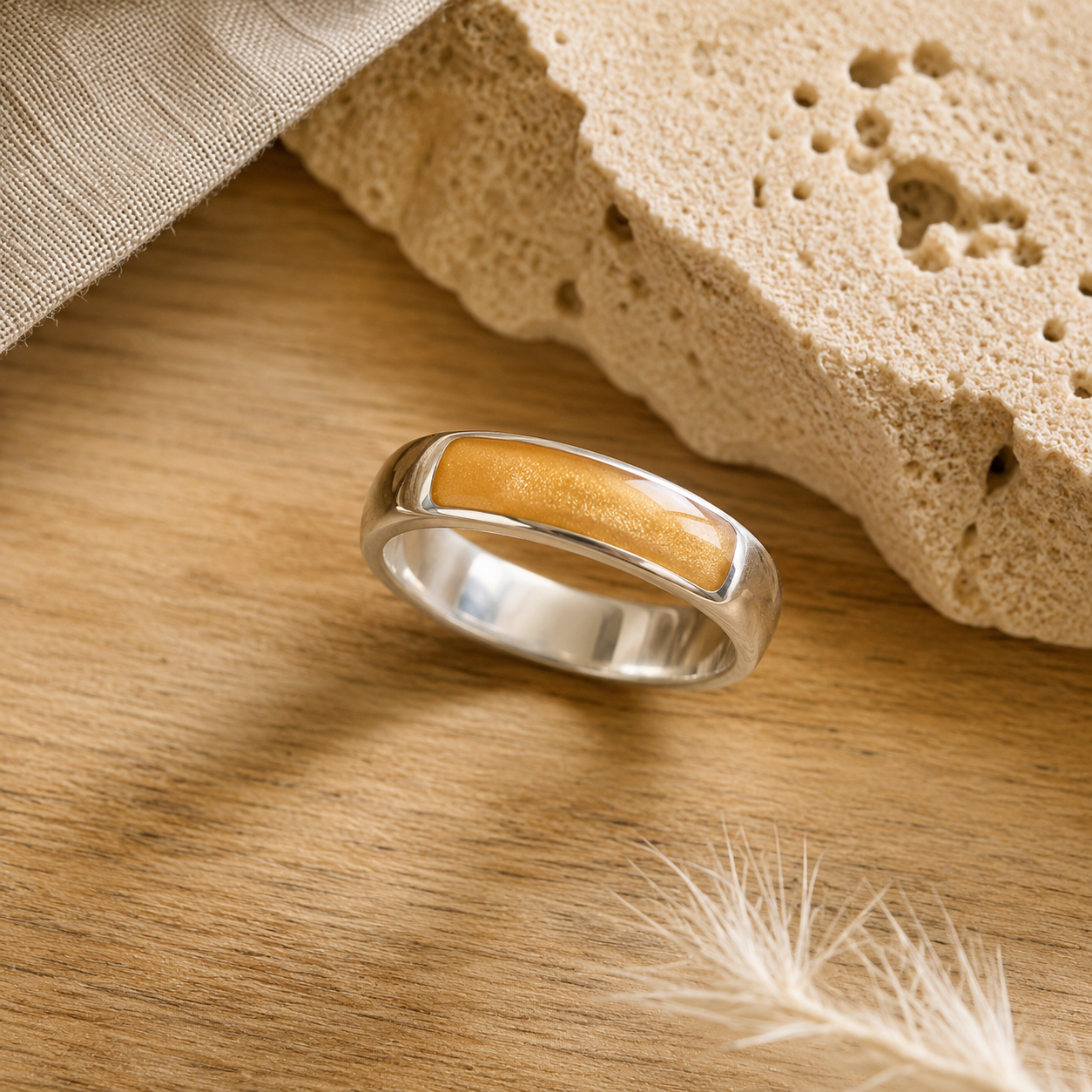 Silver mens ashes ring with gold resin inset for ashes, fur and hair on a wooden surface with a stone and feather.