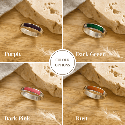 Four silver mens ashes rings with different colored resin bands on a wooden surface.