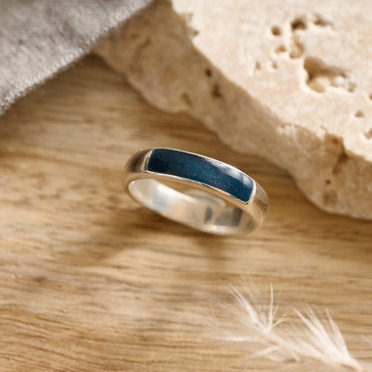 Silver memorial ring for men with navy resin inset on a wooden surface with stone and feather