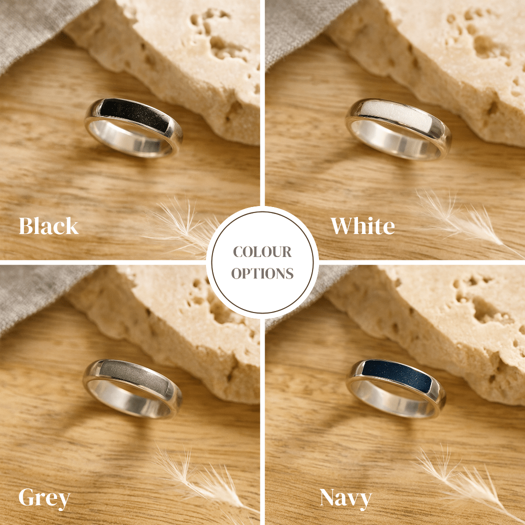 Four silver ashes rings with a resin band in black, white, gray, and navy on a wooden surface with sand and feathers.