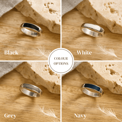 Four silver ashes rings with a resin band in black, white, gray, and navy on a wooden surface with sand and feathers.