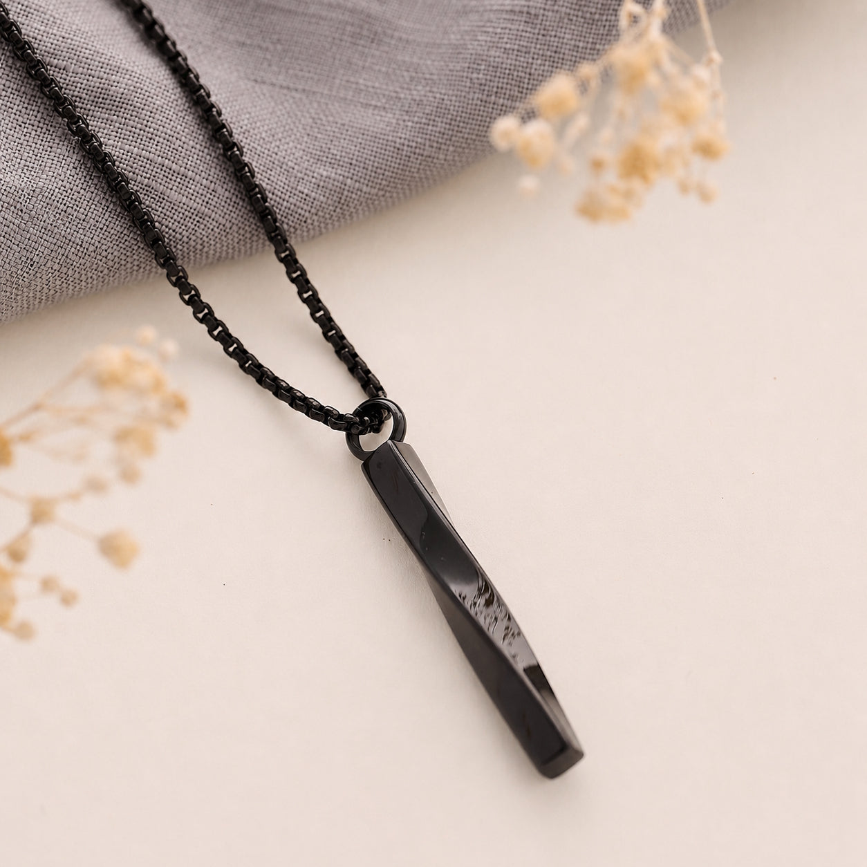 Black twist cremation necklace on a light surface with dried flowers