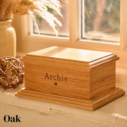 Personalised pet cremation urn crafted from oak wood. The oak urn sits on a windowsill. It has the name Archie and a pawprint engraved on it.
