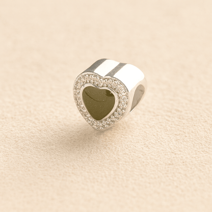 Heart-shaped silver ashes charm with a sage resin infill on a beige background