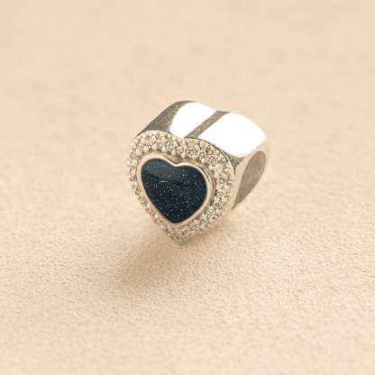 Sterling Silver Heart-shaped ashes charm with a navy resin infill and CZ crystals surround on a beige background