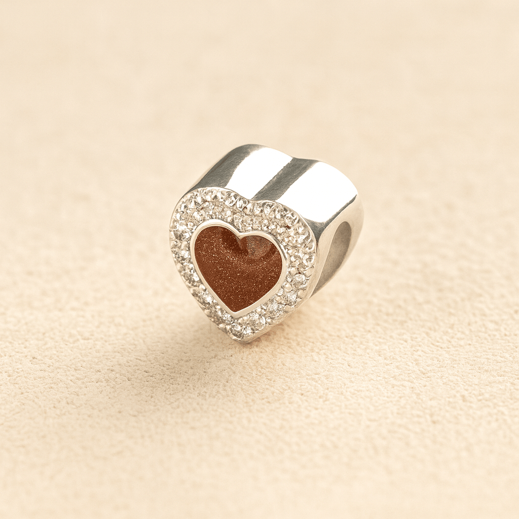 Silver heart-shaped Pandora cremation charm with a mocha resin center on a beige background