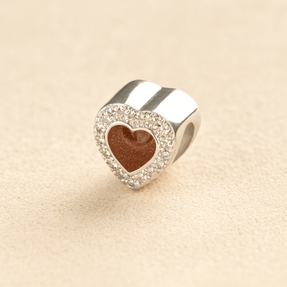 Silver heart-shaped Pandora cremation charm with a mocha resin center on a beige background