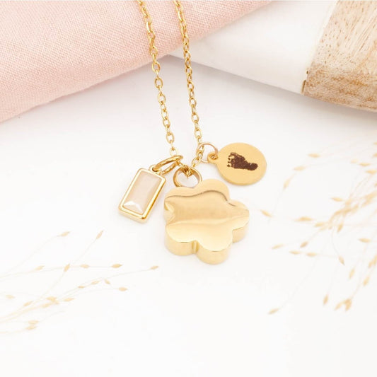 Gold footprint jewellery with heart-shaped urn necklace and birthstone charm on a light background