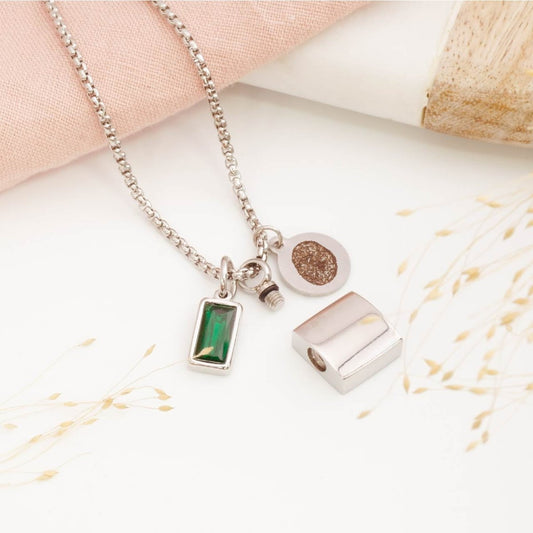 Silver fingerprint necklace for men with urn necklace and birthstone charm on a light surface