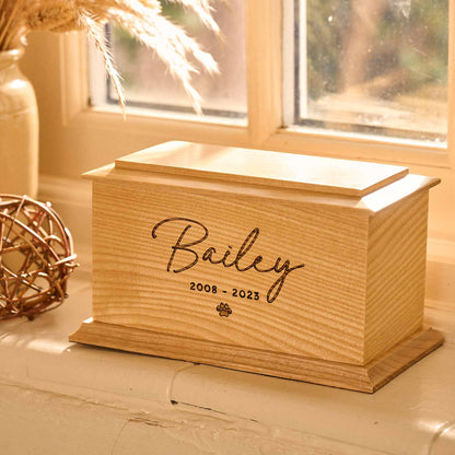 A cremation urn for pet ashes sitting on a windowsill. The urn is engraved with a pawprint. It is a dog urn or a cat urn.
