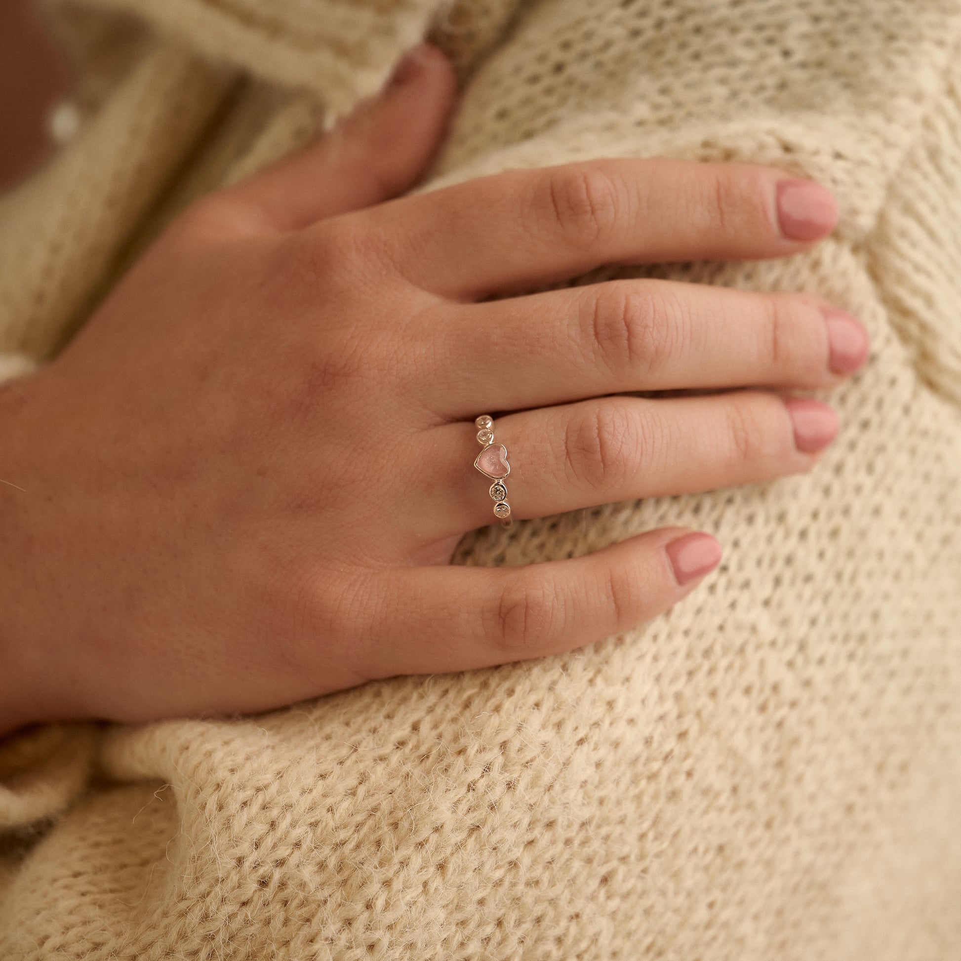 Woman wearing a pink heart cremation ashes ring with crystals while gently holding her arm