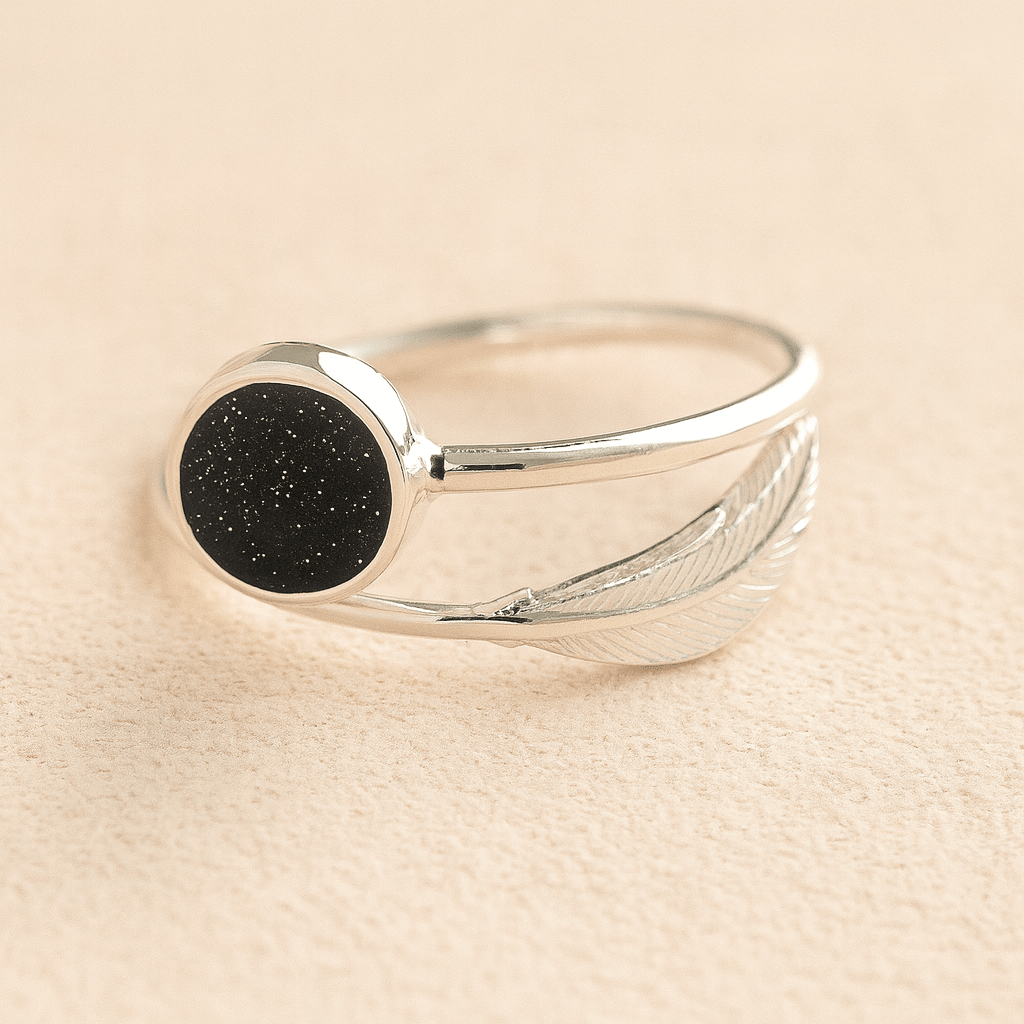Silver adjustable feather ashes ring with a black resin on a beige background