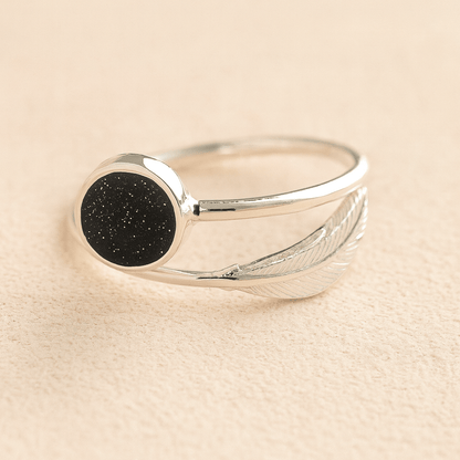 Silver adjustable feather ashes ring with a black resin on a beige background