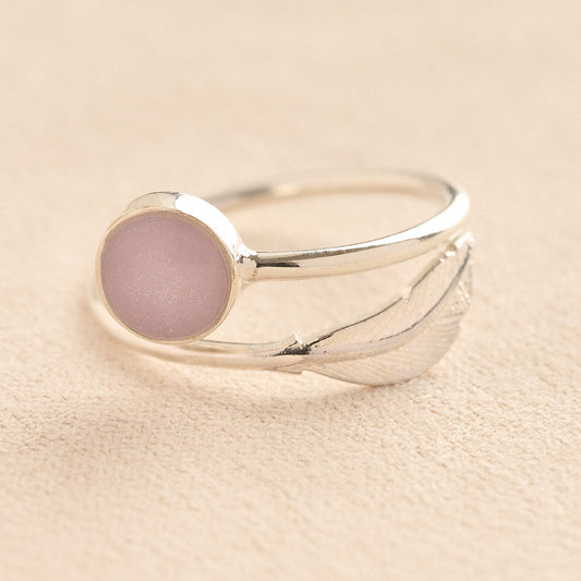 Adjustable Silver ashes ring with a lavender resin and feather on a beige background