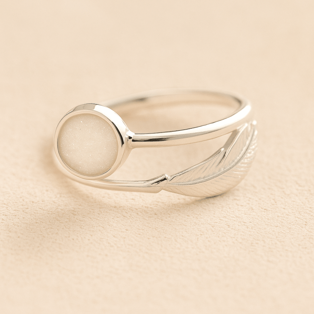 Silver adjustable feather ring with ashes and a white resin on a beige background