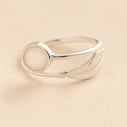 Silver adjustable feather ring with ashes and a white resin on a beige background
