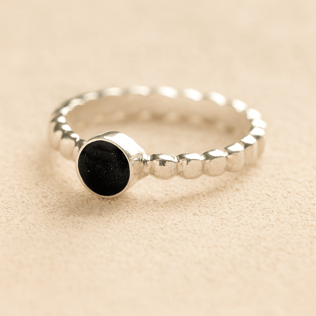 Silver bubble cremation ring with black resin on a beige background.