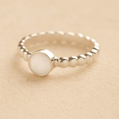 Silver bubble memorial ring with white resin on a beige background.
