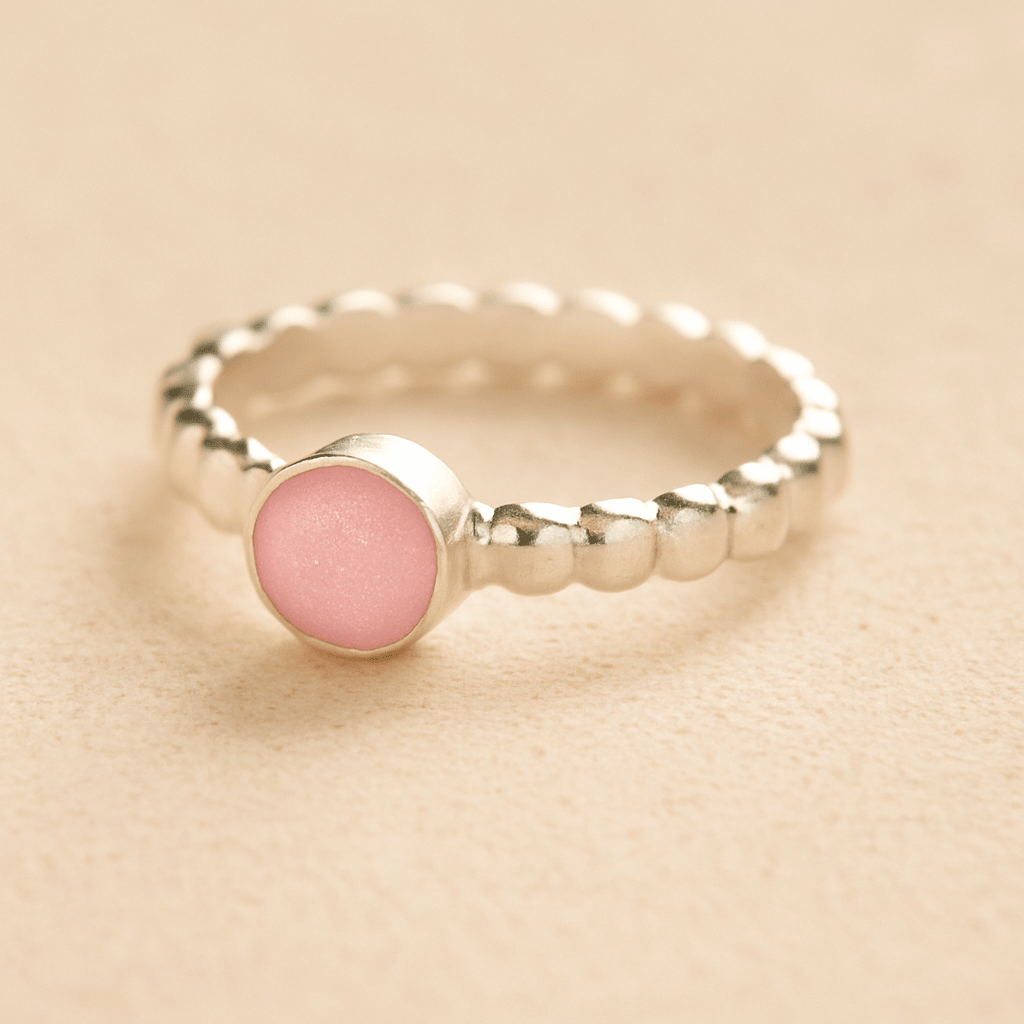 Silver bubble memorial ring with light pink resin on a beige background.