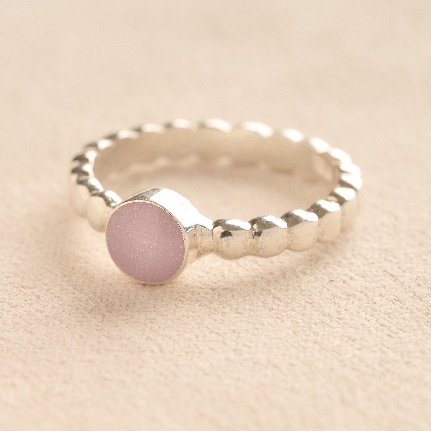 Silver bubble ashes ring with lavender resin on a beige background.