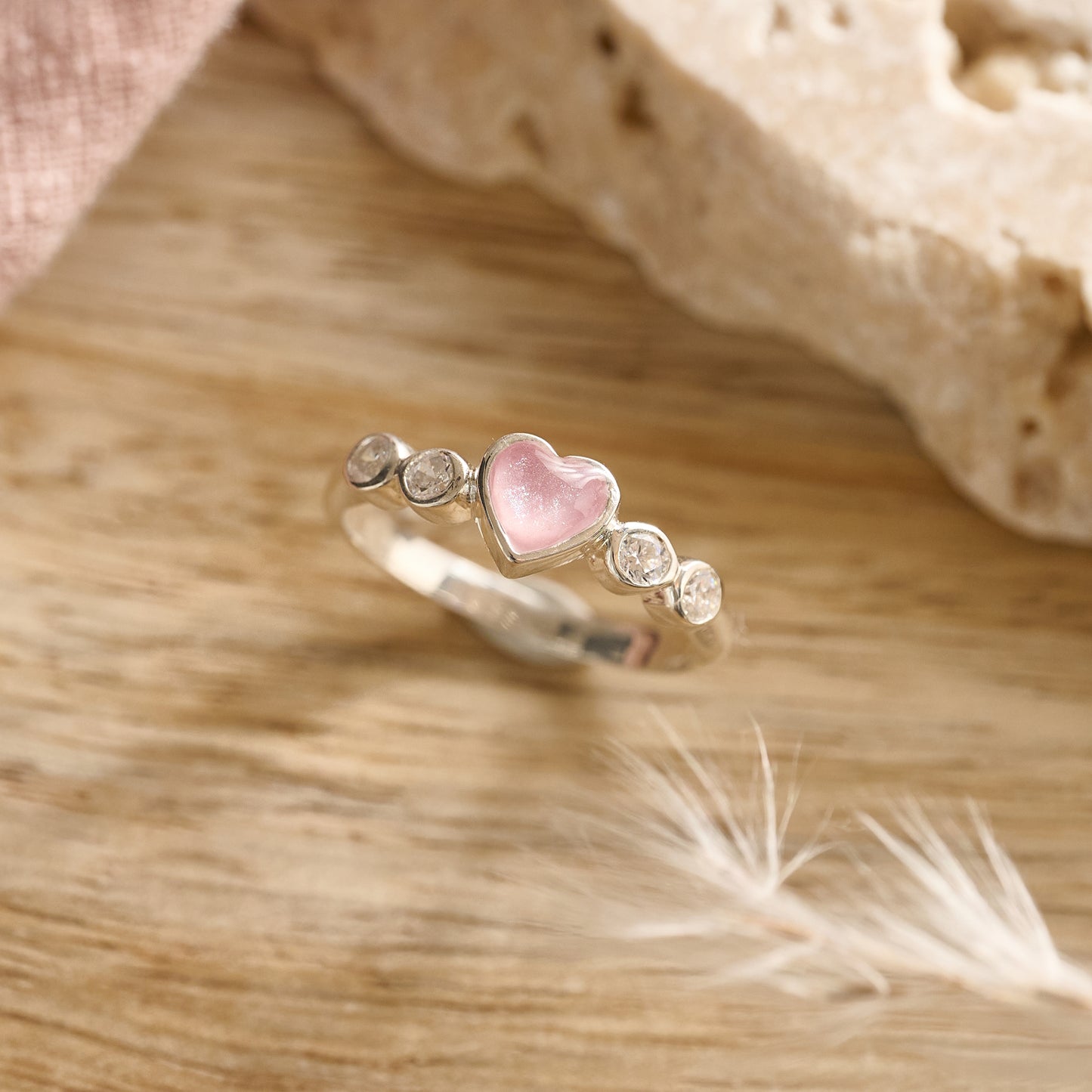 Flatlay of sterling silver heart cremation ring with pink resin and crystals on wooden background