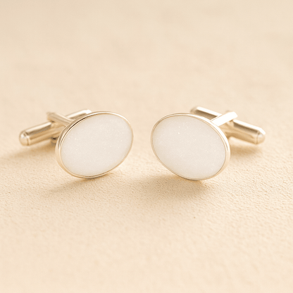 Silver oval cremation ashes cufflinks with a white resin infill made with ashes or fur on a beige background