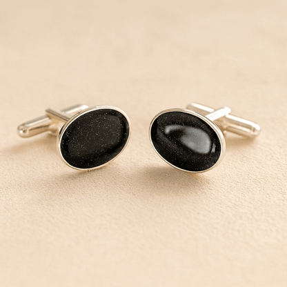 Silver oval ashes cufflinks with a black resin infill made with ashes or fur on a beige background
