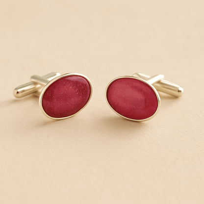 Silver oval memorial cufflinks with a dark pink resin infill made with ashes or fur on a beige background