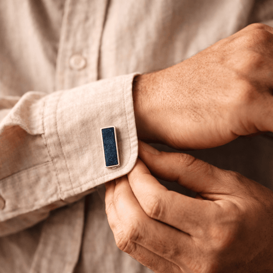 Man adjusting an ashes cufflink on a beige shirt sleeve.