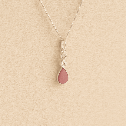 Silver Cremation ashes necklace with a teardrop pendant and dark pink resin filled with ashes or fur, displayed on a soft beige background – suitable for pet or human memorials.