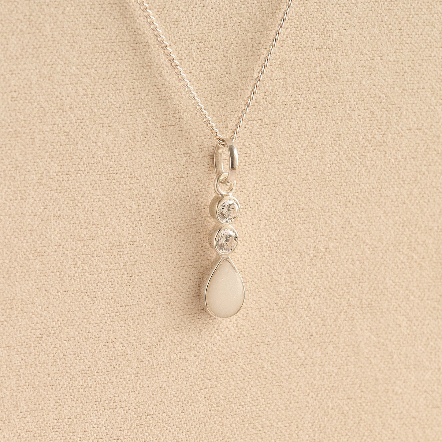 Silver Cremation ashes necklace with a teardrop pendant and white resin filled with ashes or fur, displayed on a soft beige background – suitable for pet or human memorials.