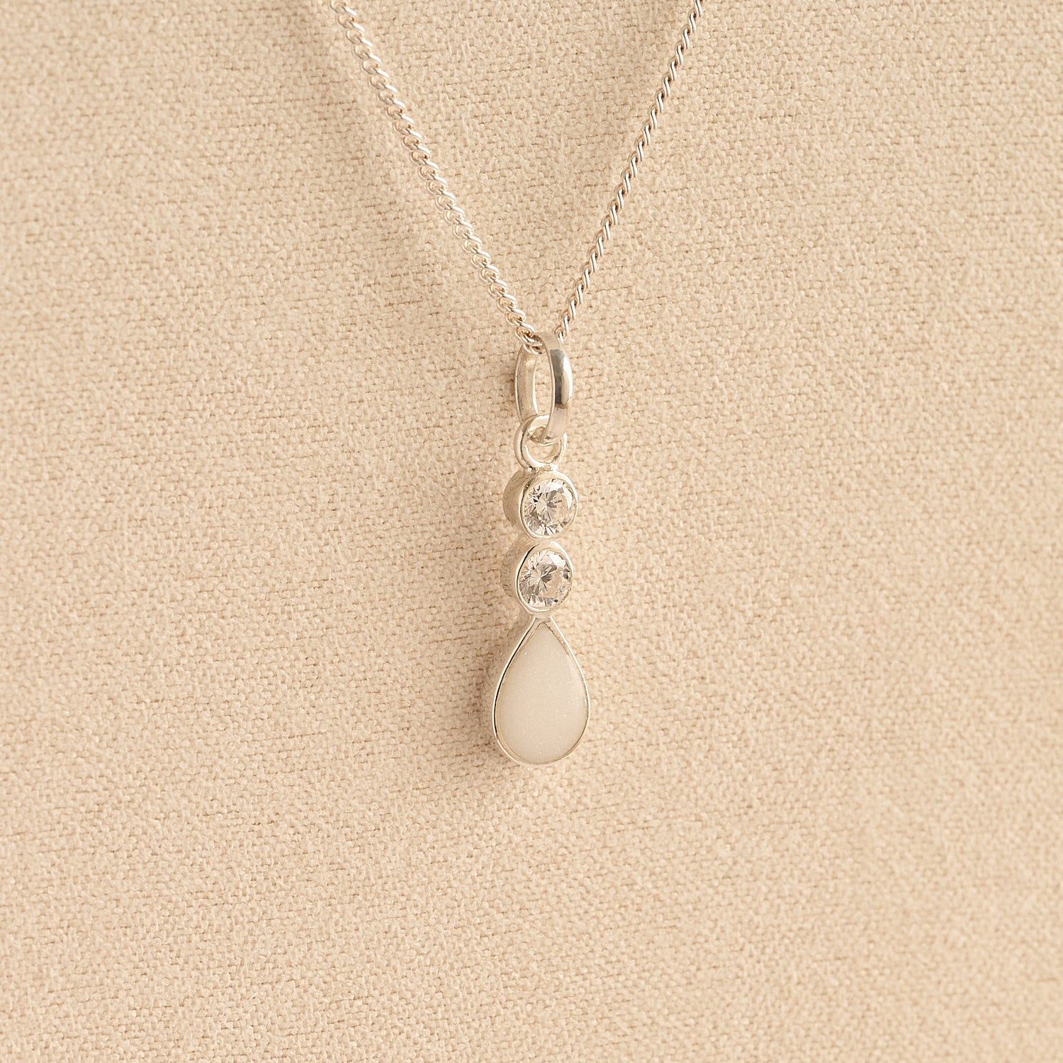 Silver Cremation ashes necklace with a teardrop pendant and white resin filled with ashes or fur, displayed on a soft beige background – suitable for pet or human memorials.