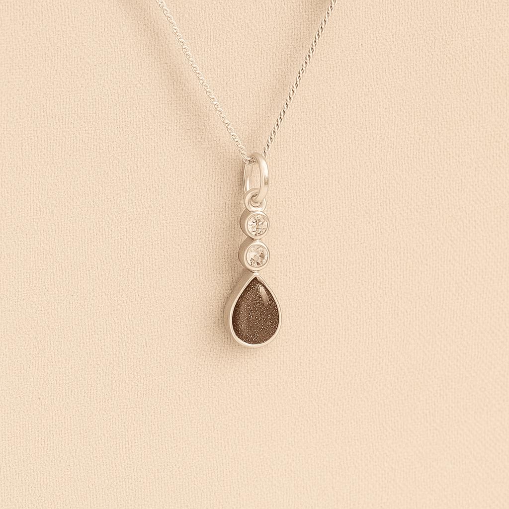 Silver Cremation ashes necklace with a teardrop pendant and mocha resin filled with ashes or fur, displayed on a soft beige background – suitable for pet or human memorials.