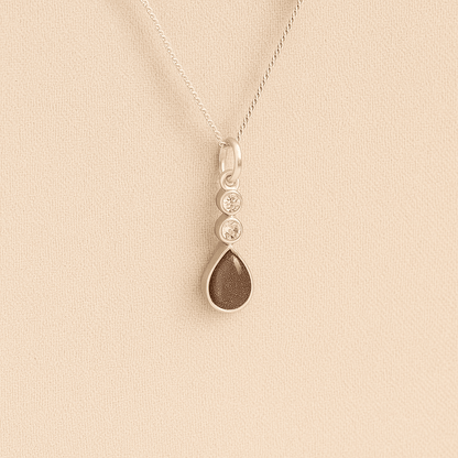 Silver Cremation ashes necklace with a teardrop pendant and mocha resin filled with ashes or fur, displayed on a soft beige background – suitable for pet or human memorials.