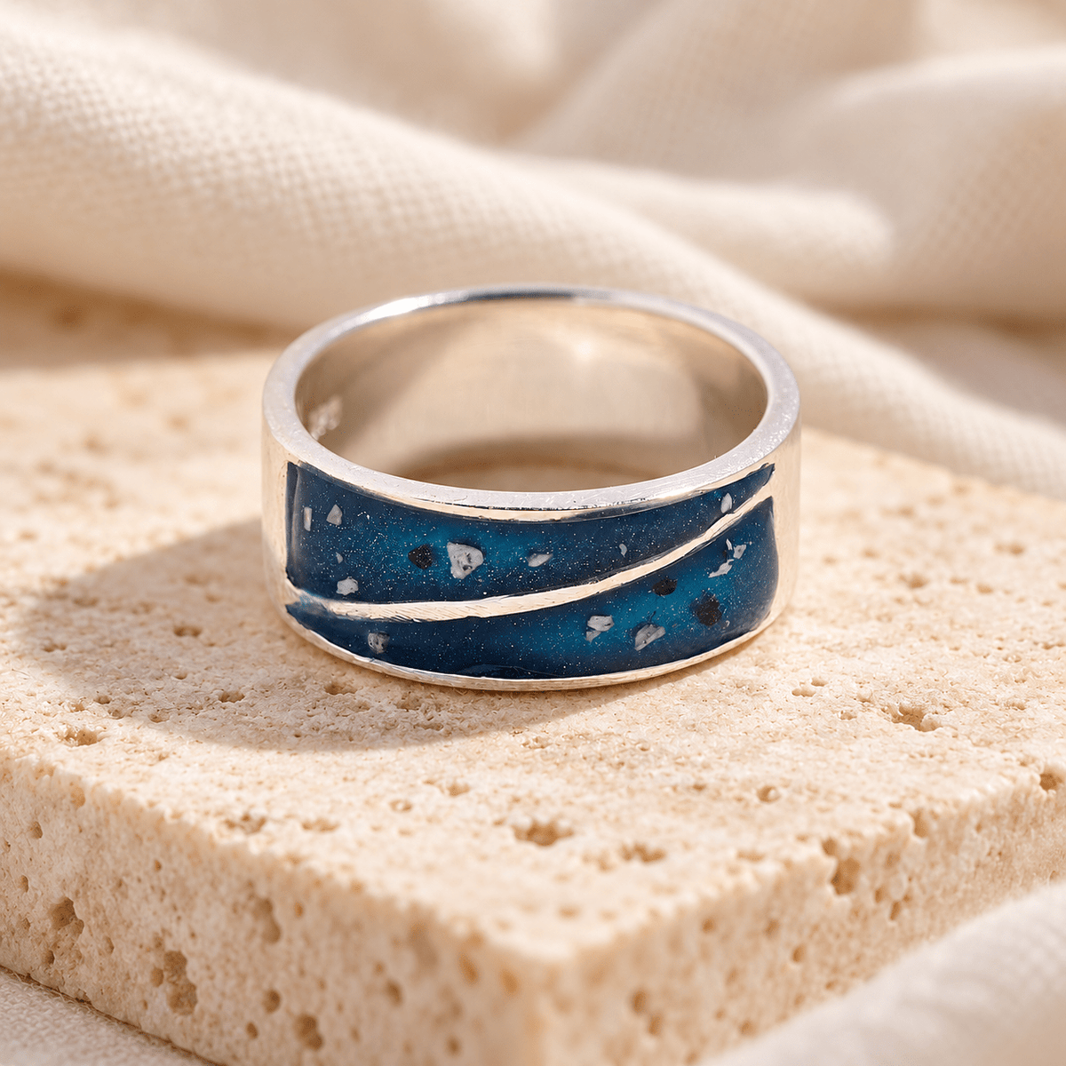 Wide sterling silver duo triangle ashes ring with two deep blue resin sections containing visible ashes, divided by a sweeping silver line, on cream stone.